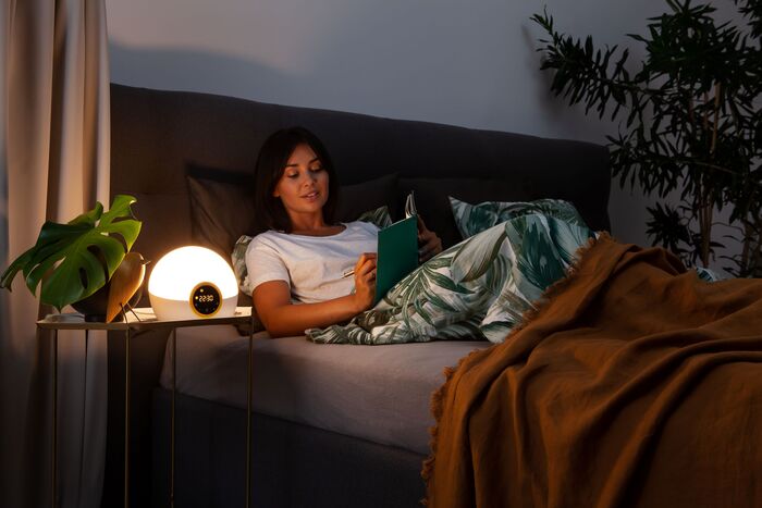 Writing in a journal whilst in bed on an evening beside a table with a Lumie Bodyclock Rise 100 Wake-Up Light